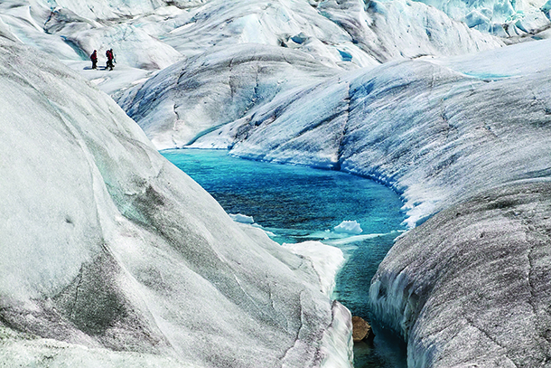 Two people hiking on glacial ice cap near blue pools of water
